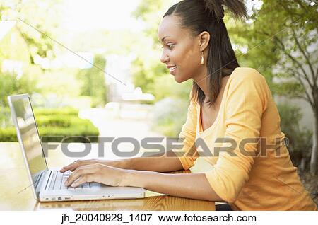 Young woman working on a laptop smiling View Large Photo Image Stock Photo - Young woman working on a laptop smiling. Fotosearch