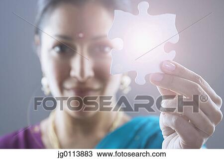 Stock Image - Close-up of a mid adult woman holding a jigsaw piece. Fotosearch