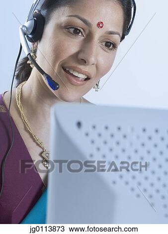 Stock Image - Close-up of a mid adult woman wearing headset in front of a computer. Fotosearch