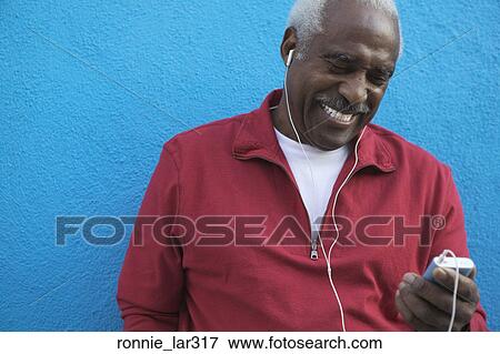 Mature man standing against a wall and listening to music View Large Photo Image Stock Photo - Mature man standing against a wall and listening to music. Fotosearch