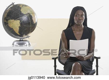 Mid adult woman sitting on a chair holding a document near a globe View Large Photo Image Stock Image - Mid adult woman sitting on a chair holding a document near a globe. Fotosearch