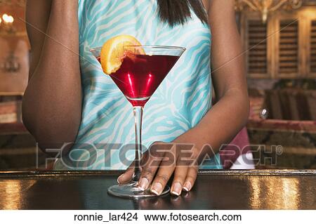 Picture - Mid section view of a young woman standing at a bar counter with a martini glass. Fotosearch