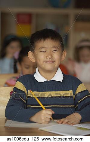 Stock Photograph - Portrait of a boy holding a pencil and smiling in a classroom. Fotosearch