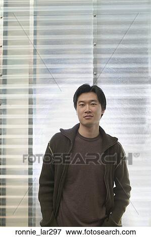 Stock Photo - Portrait of a young man standing with his hands in his pockets. Fotosearch