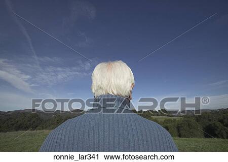 Stock Image - Rear view of a senior man standing in a field. Fotosearch