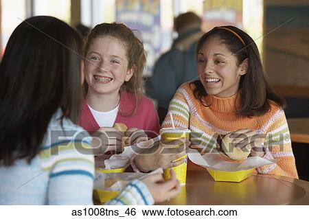 Three teenage girls sitting at a table and eating View Large Photo Image Stock Photograph - Three teenage girls sitting at a table and eating. Fotosearch
