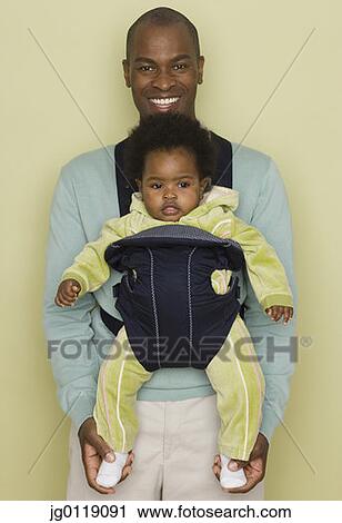 Stock Image - Father carrying baby daughter in carrier. Fotosearch