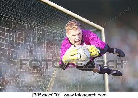 Stock Image - Male goalie catching ball in midair. Fotosearch