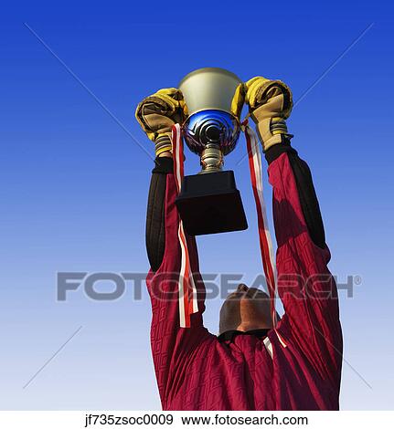 Stock Photo - Male goalie triumphantly holding up trophy. Fotosearch