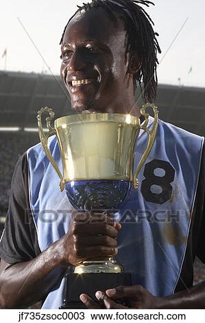 Stock Image - Male soccer player proudly holding trophy. Fotosearch