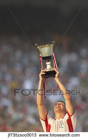 Male soccer player triumphantly holding up trophy View Large Photo Image Stock Image - Male soccer player triumphantly holding up trophy. Fotosearch