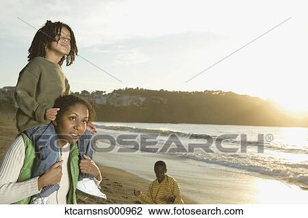 Mother carrying her son on her shoulders at the beach View Large Photo Image Stock Image - Mother carrying her son on her shoulders at the beach. Fotosearch