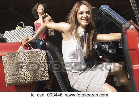 Stock Photograph - Two women getting out of convertible after shopping. Fotosearch