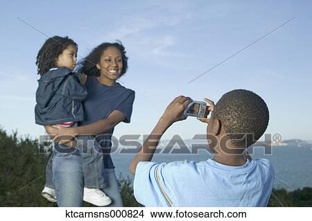 Young boy taking a picture of his mother and sister View Large Photo Image Picture - Young boy taking a picture of his mother and sister. Fotosearch