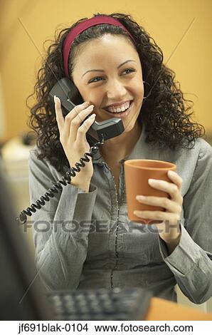 Picture - Young businesswoman drinking coffee and talking on the phone. Fotosearch
