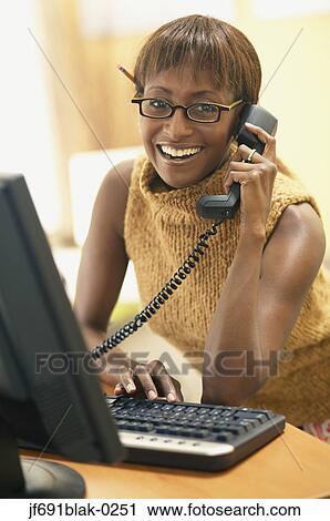 Stock Image - Young businesswoman talking on the phone while working. Fotosearch
