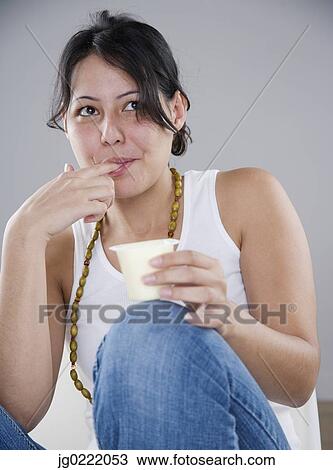 Stock Image - Young woman eating pudding with her fingers. Fotosearch