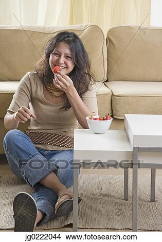 Young woman eating strawberries on living room floor View Large Photo Image Picture - Young woman eating strawberries on living room floor. Fotosearch
