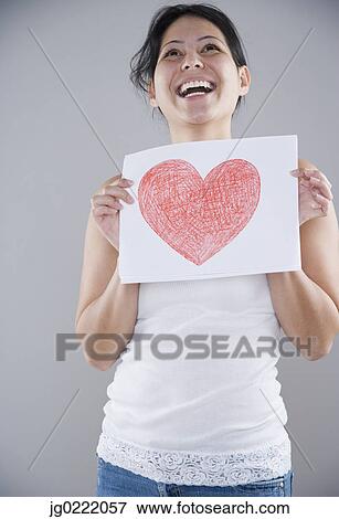 Young woman holding a piece of paper with a heart drawn on it View Large Photo Image Stock Photo - Young woman holding a piece of paper with a heart drawn on it. Fotosearch