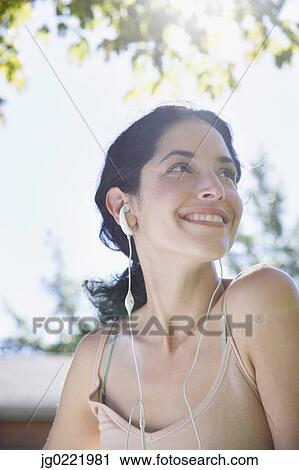 Stock Image - Young woman listening to earbuds. Fotosearch
