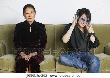 Stock Image - Young woman listening to music beside her stern mother. Fotosearch