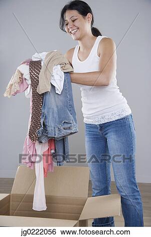 Stock Photograph - Young woman piling clothes into a cardboard box. Fotosearch
