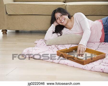 Stock Photograph - Young woman playing backgammon on living room floor. Fotosearch