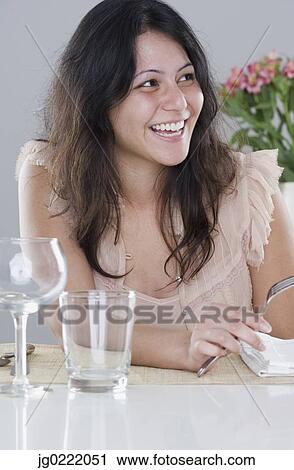 Stock Image - Young woman sitting at the dinner table. Fotosearch