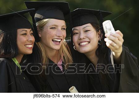 Young women taking pictures of themselves with a camera phone on Graduation Day View Large Photo Image Picture - Young women taking pictures of themselves with a camera phone on Graduation Day. Fotosearch