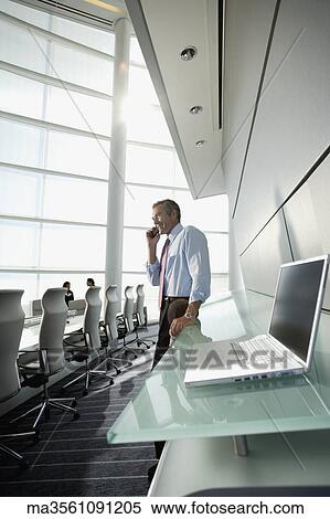 Stock Photography - Businessman talking on cell phone in conference room. Fotosearch