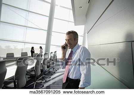 Stock Photography - Businessman talking on cell phone in conference room. Fotosearch