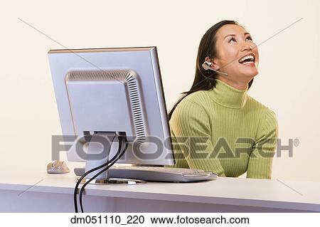 Stock Image - Businesswoman laughing and talking on phone in front of computer. Fotosearch