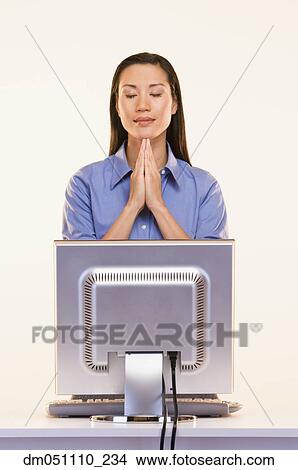 Picture - Businesswoman praying in front of computer. Fotosearch