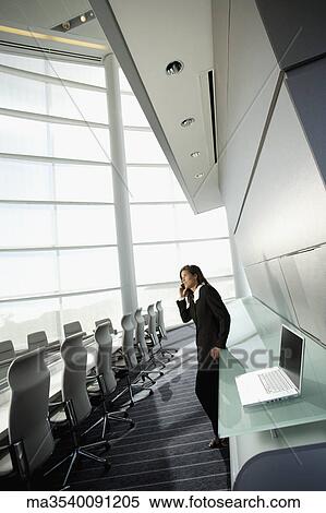 Stock Photography - Businesswoman talking on cell phone in conference room. Fotosearch