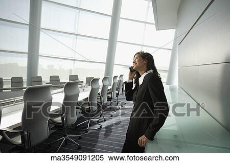 Stock Photography - Businesswoman talking on cell phone in conference room. Fotosearch