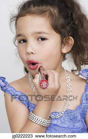 Stock Image - Portrait of girl applying makeup while playing dress up. Fotosearch