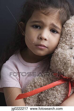 Stock Photo - Portrait of girl crying and hugging teddy bear. Fotosearch