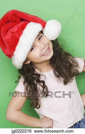 Stock Photograph - Portrait of girl smiling while wearing santa hat. Fotosearch