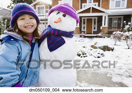 Picture - Portrait of girl with snowman in front yard. Fotosearch