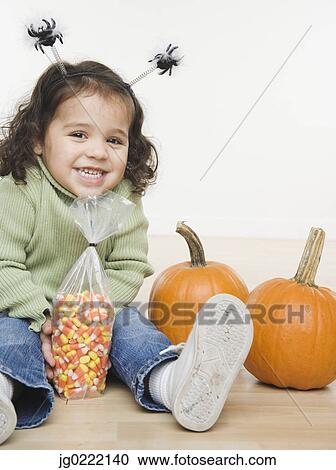 Stock Image - Portrait of little girl with pumpkins and candy corn. Fotosearch