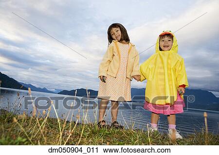 Stock Image - Portrait of sisters holding hands at lake. Fotosearch