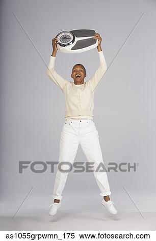 Stock Photography - Portrait of woman jumping in air holding scale . Fotosearch