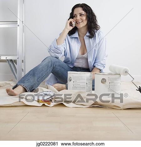 Stock Image - Portrait of woman sitting on floor while taking on phone. Fotosearch