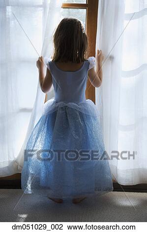 Stock Image - Rear view of girl dressed as princess and looking out window. Fotosearch