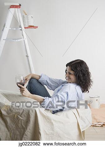 Stock Image - Woman drinking wine while painting. Fotosearch