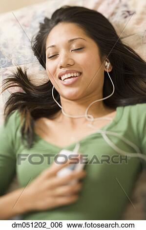 Stock Photograph - Woman laying on bed listening to music. Fotosearch
