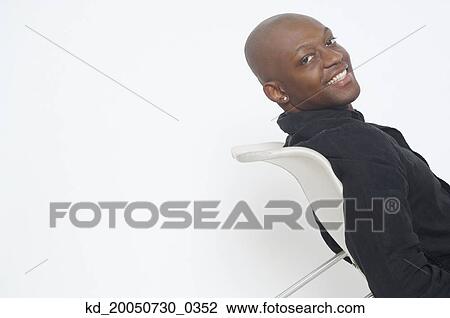 Young man smiling for the camera in chair View Large Photo Image Stock Image - Young man smiling for the camera in chair. Fotosearch