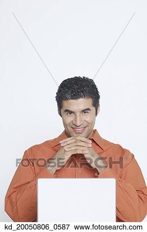 Young man smiling for the camera while using a laptop View Large Photo Image Stock Photo - Young man smiling for the camera while using a laptop. Fotosearch