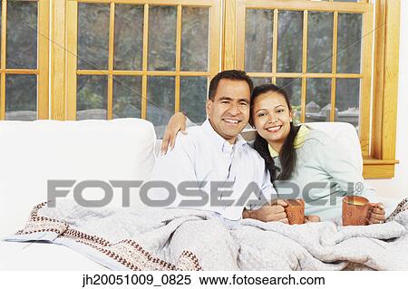 Stock Photography - Couple sitting on the couch under a blanket together. Fotosearch