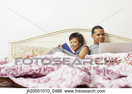 Couple using a laptop in bed View Large Photo Image Stock Photo - Couple using a laptop in bed. Fotosearch